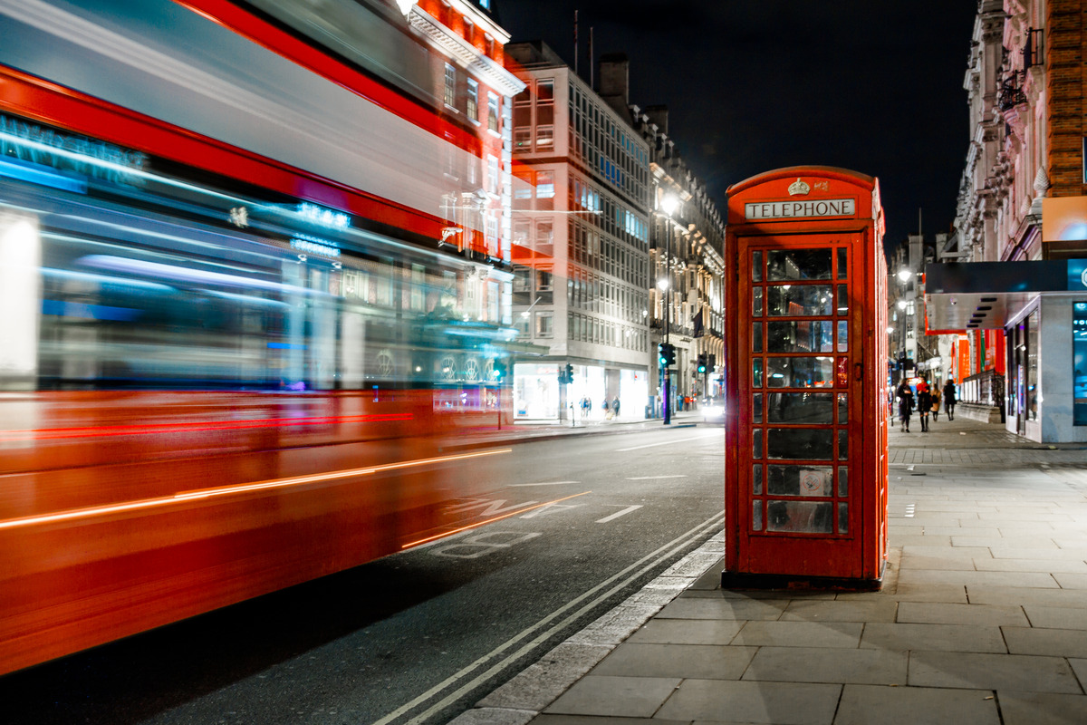 a bus rushing past a london phone box at night