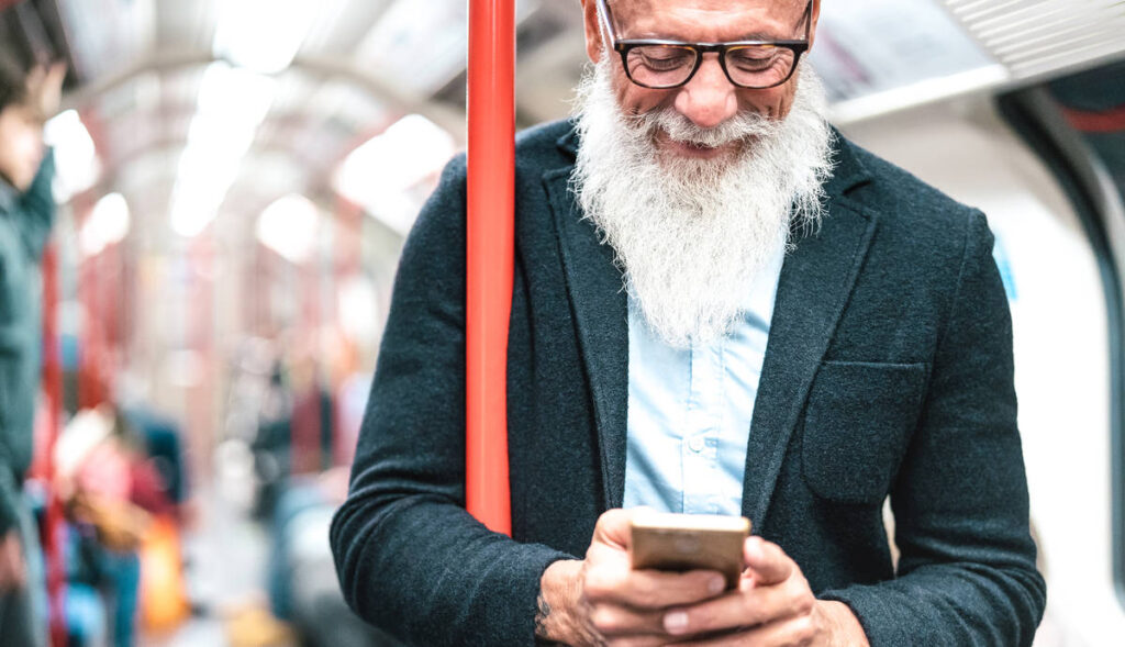 a kind bearded man smiling at his phone on the Tube