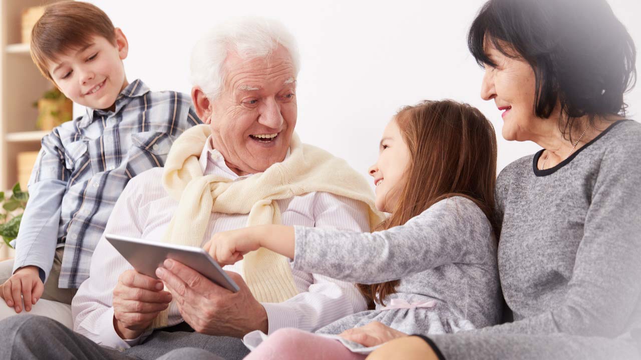 Happy grandchildren and grandparents using a tablet in living room