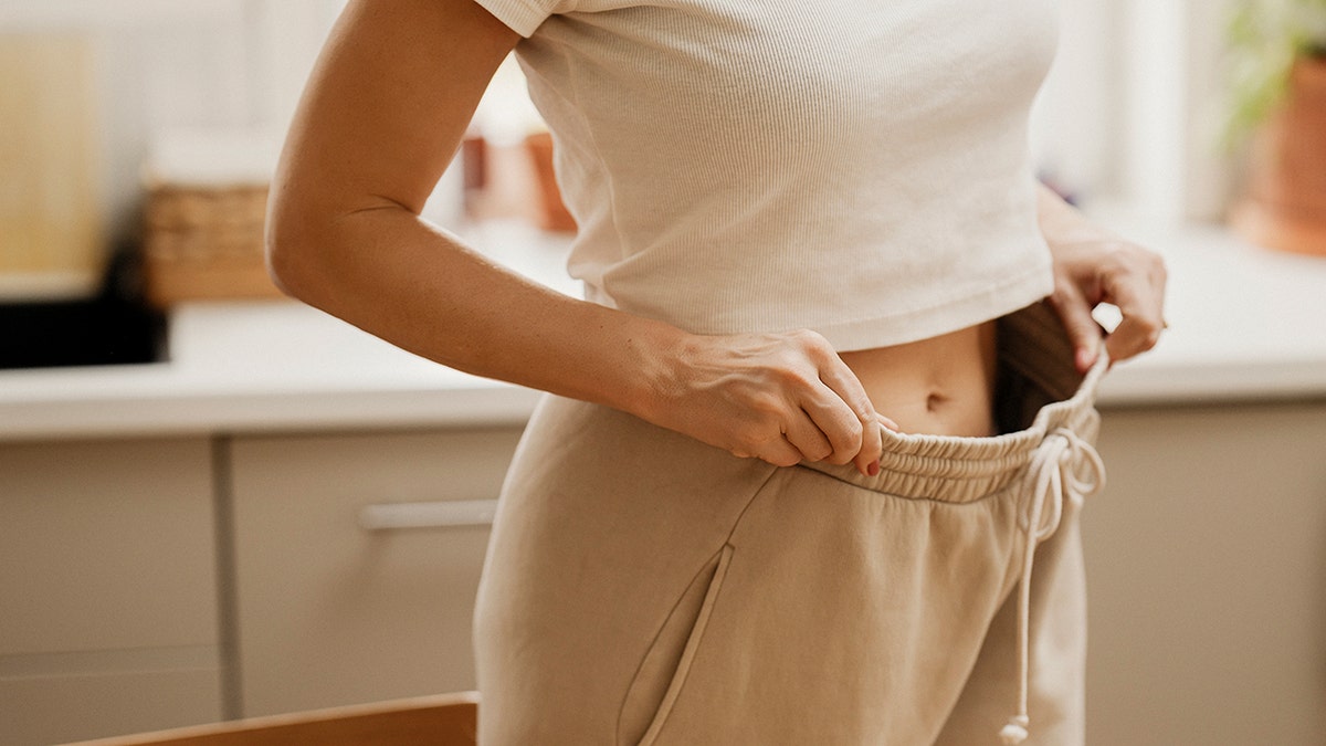 woman stretches her sweatpants out with hands showing belly