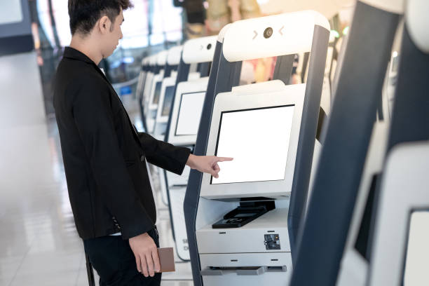 A man uses a touchscreen self-check-in kiosk at an airport, pointing at the blank display.