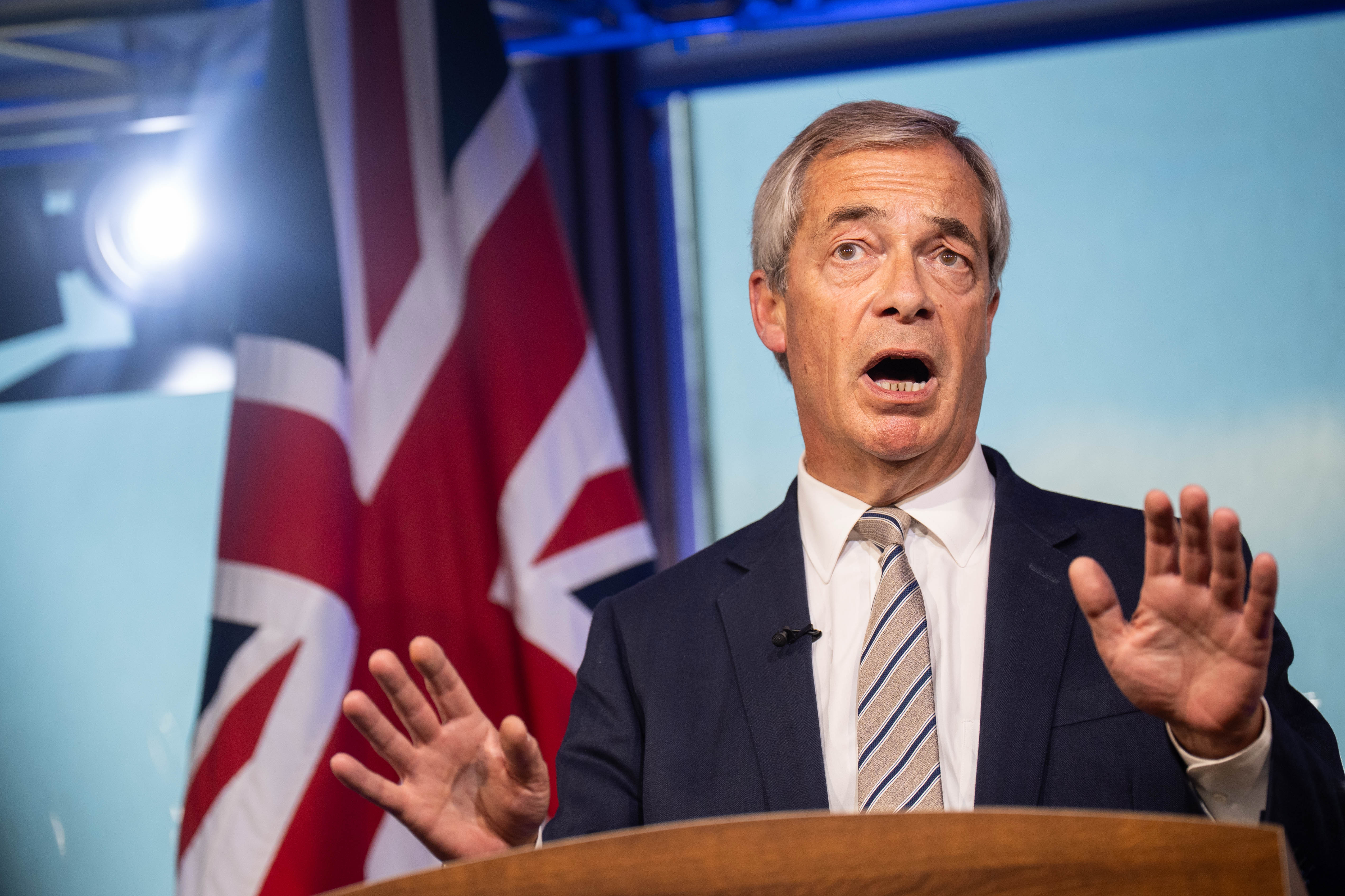 Nigel Farage reacting to Keir Starmer's speech, with a British flag in the background.