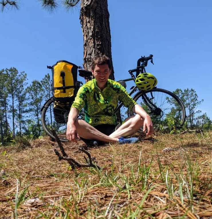 Sholto David sitting cross-legged next to his bicycle.