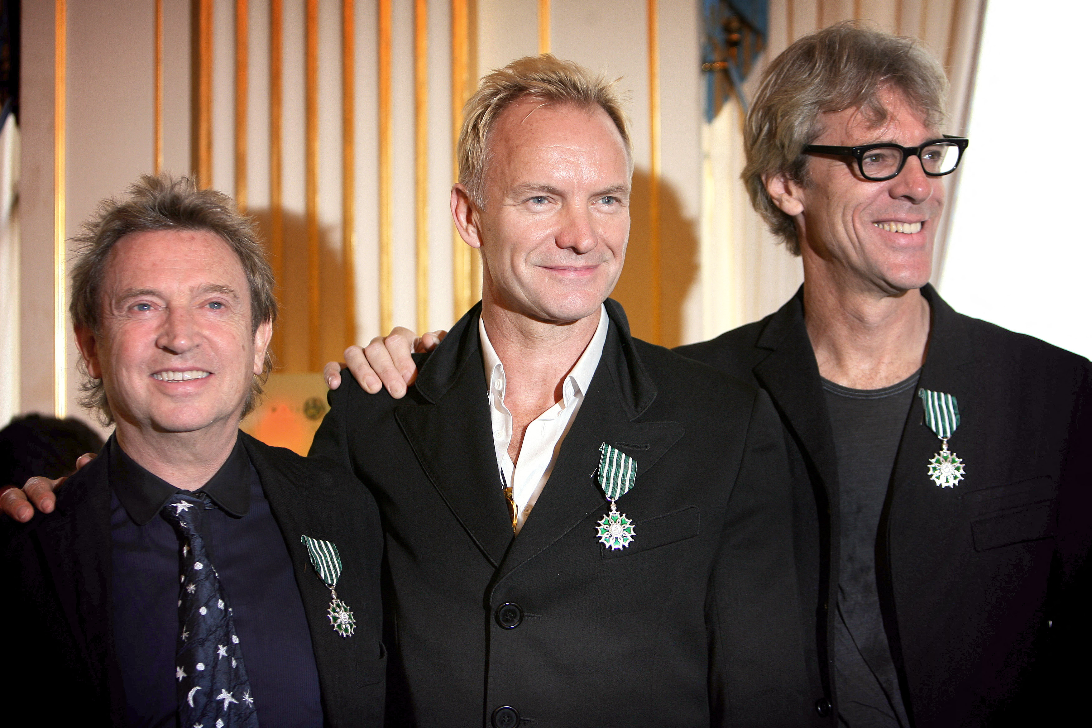 Rock band The Police members Sting, Andy Summers, and Stewart Copeland, wearing medals.