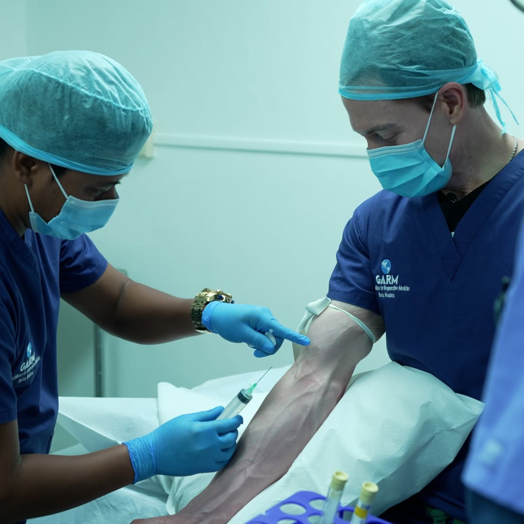 A person in scrubs and a mask injecting a substance into another person's arm.