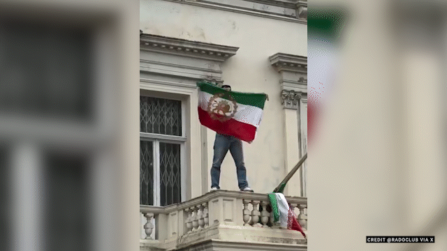 A person holding an Iranian flag while standing on a balcony.