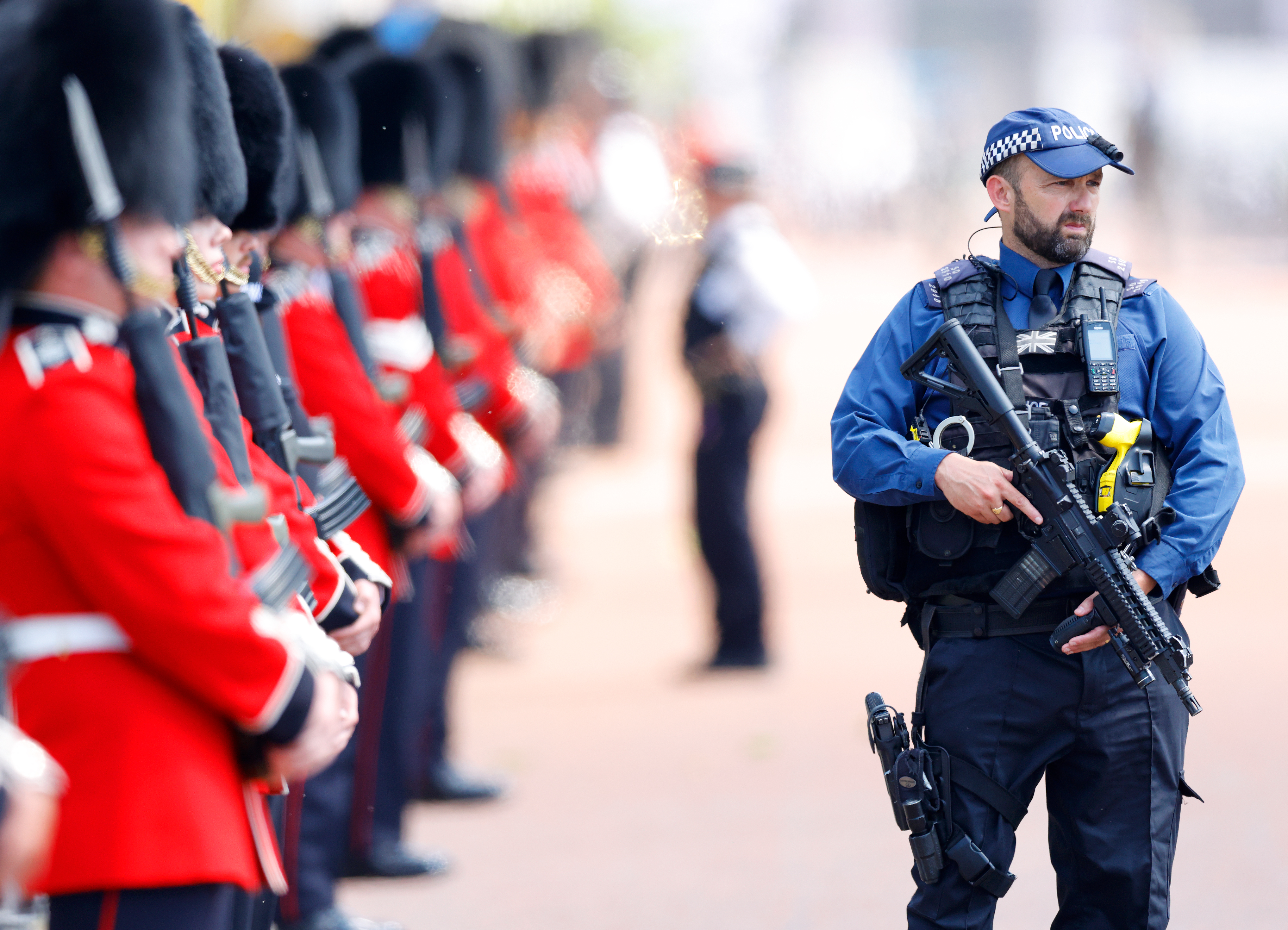 A Metropolitan Police Specialist Operations firearms officer stands ready with soldiers of The Grenadier Guards behind them.
