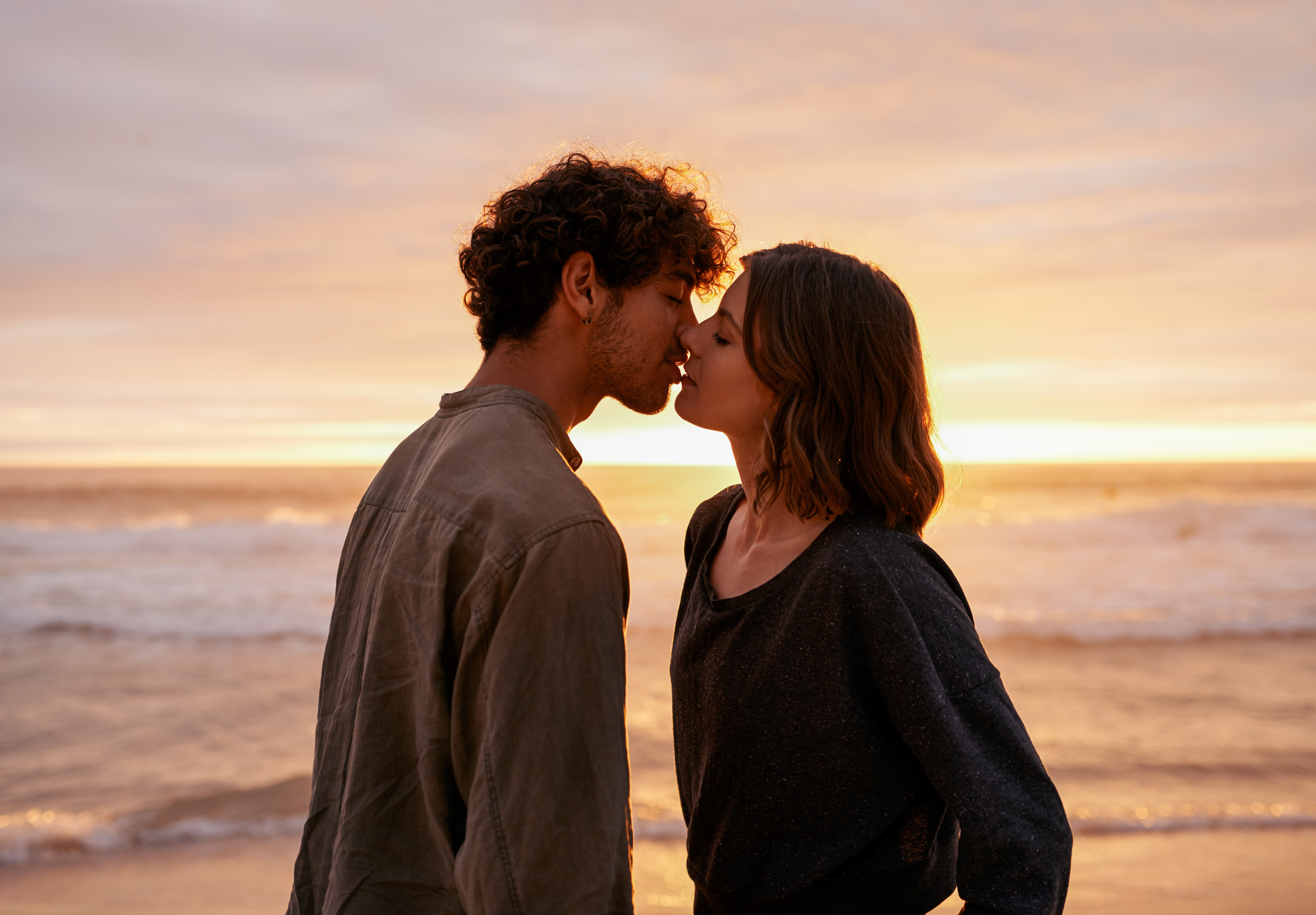 Affectionate young couple kissing on the beach at sunset.