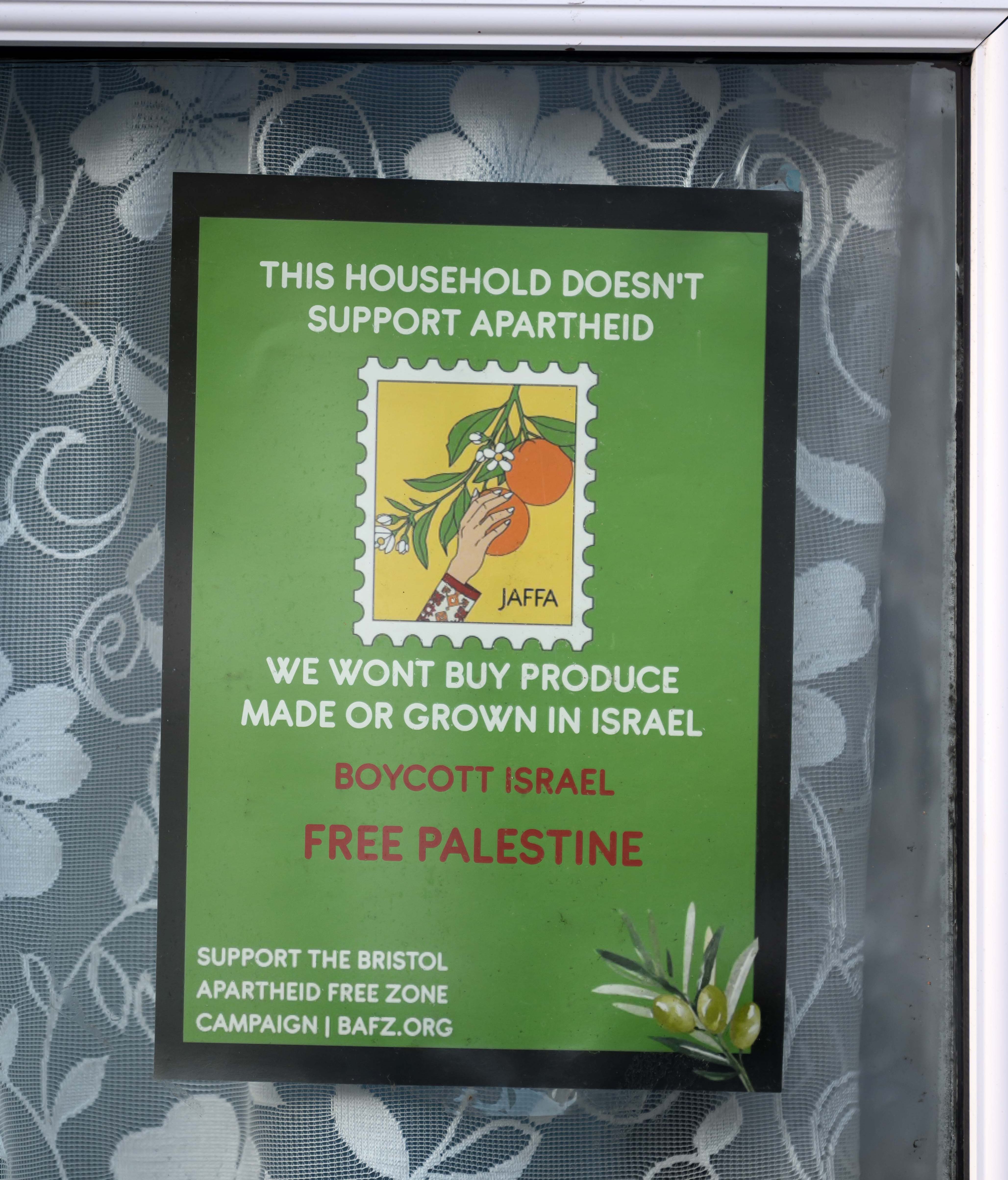 A sign on a window of a home reads, "THIS HOUSEHOLD DOESN'T SUPPORT APARTHEID," "WE WON'T BUY PRODUCE MADE OR GROWN IN ISRAEL," "BOYCOTT ISRAEL," "FREE PALESTINE," and "SUPPORT THE BRISTOL APARTHEID FREE ZONE CAMPAIGN | BAFZ.ORG."