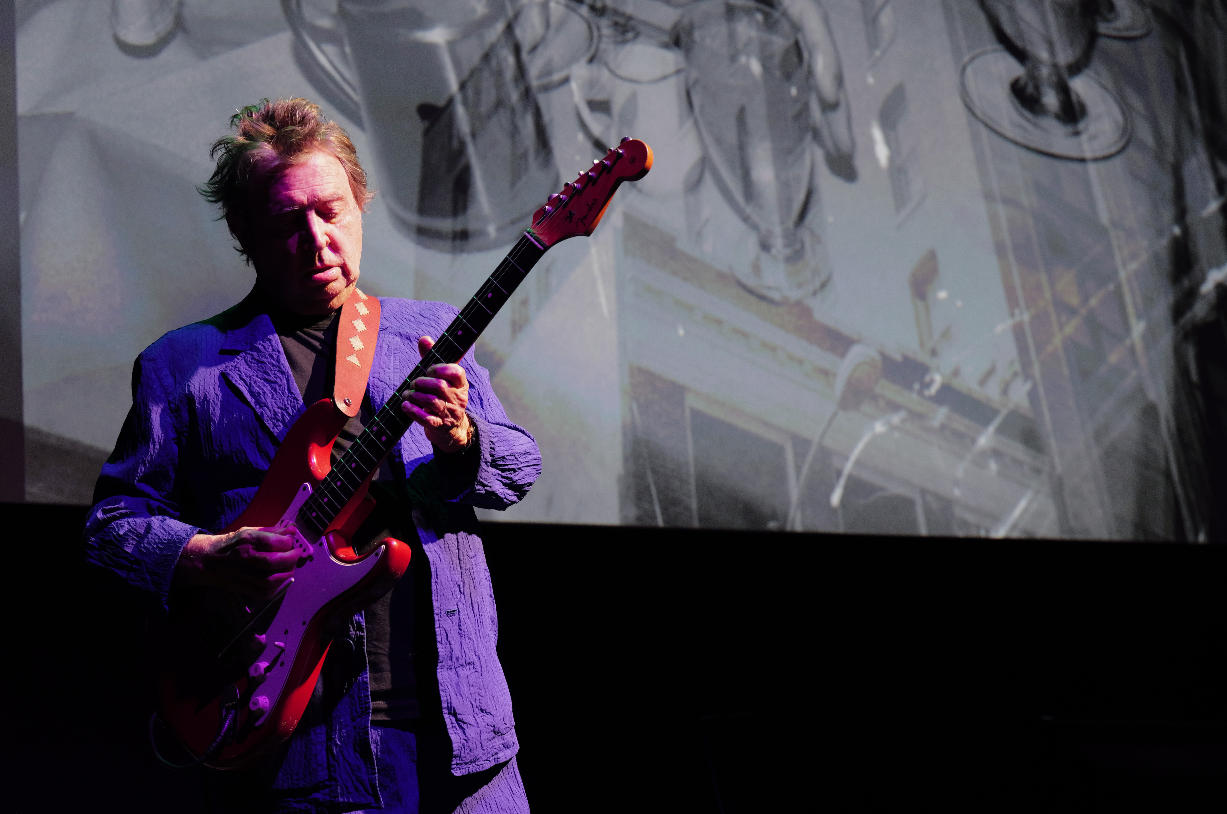 Andy Summers playing a red electric guitar on stage.
