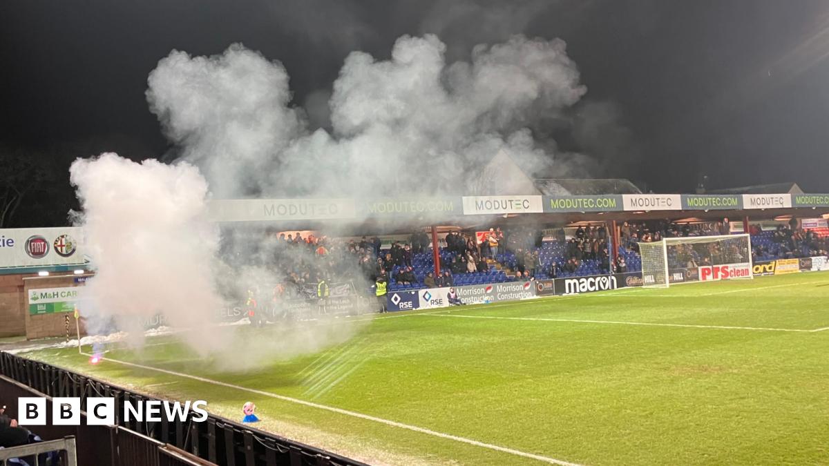 Smoke rises from the pyrotechnic as it burns near a corner flag on Ross County's pitch in Dingwall. The ground's Jail End stand is in the background.