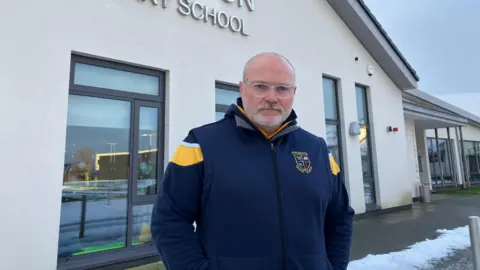 A bald man in an Ebrington zip up top stares at the camera