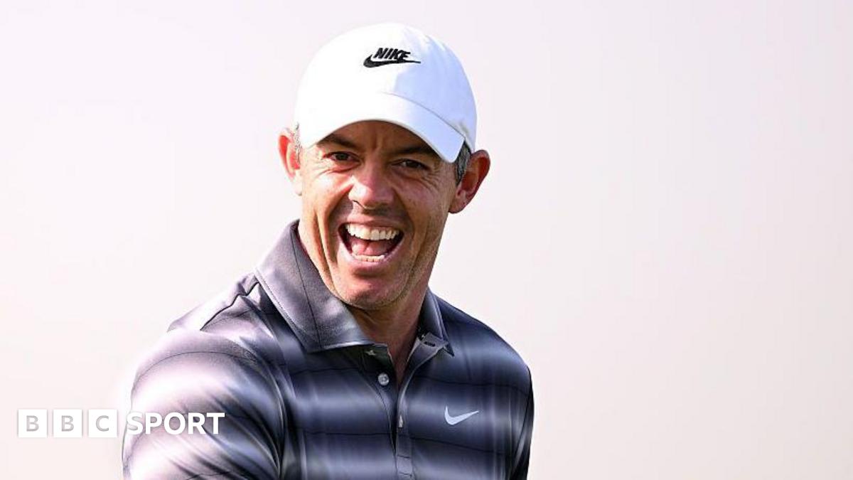 Rory McIlroy appears to be laughing while wearing a golf shirt with a black and white hooped effect, and a white cap