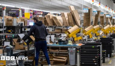 A worker at a warehouse packages items as they pass him on a conveyor belt.