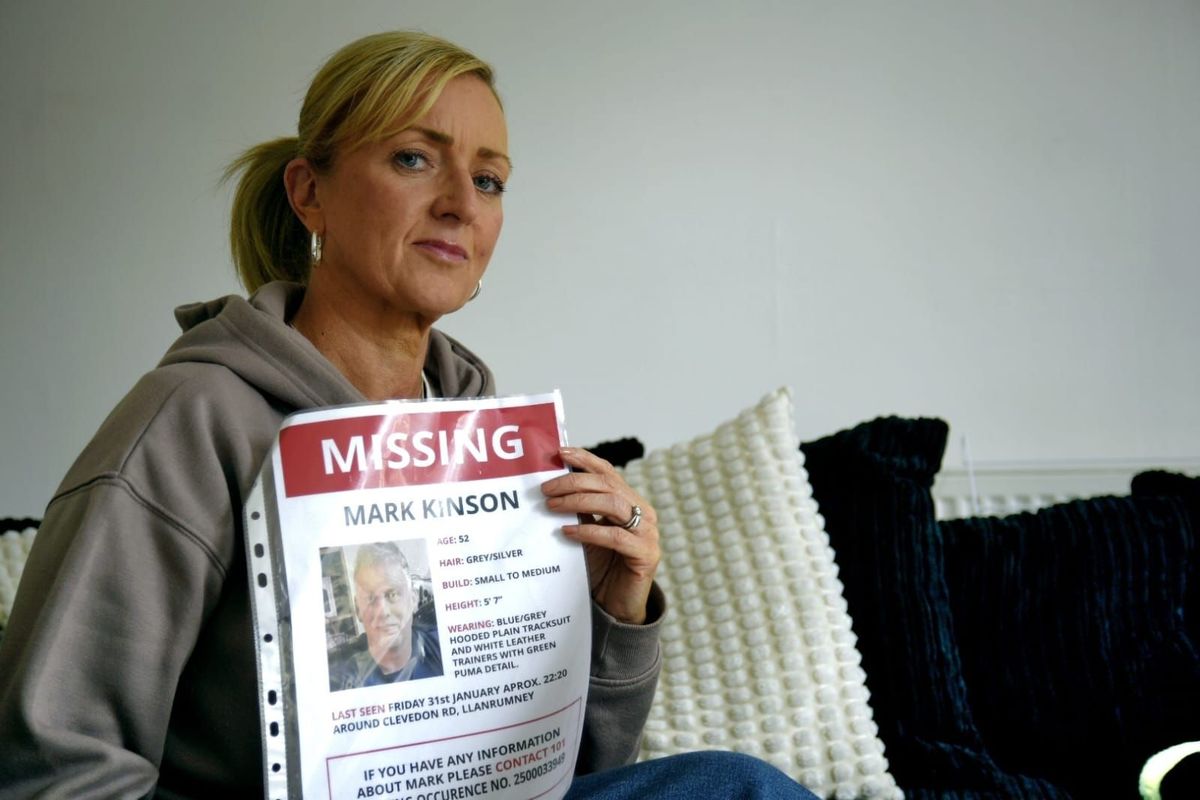 A white woman in her 50s with blonde hair. She is holding a missing person's poster