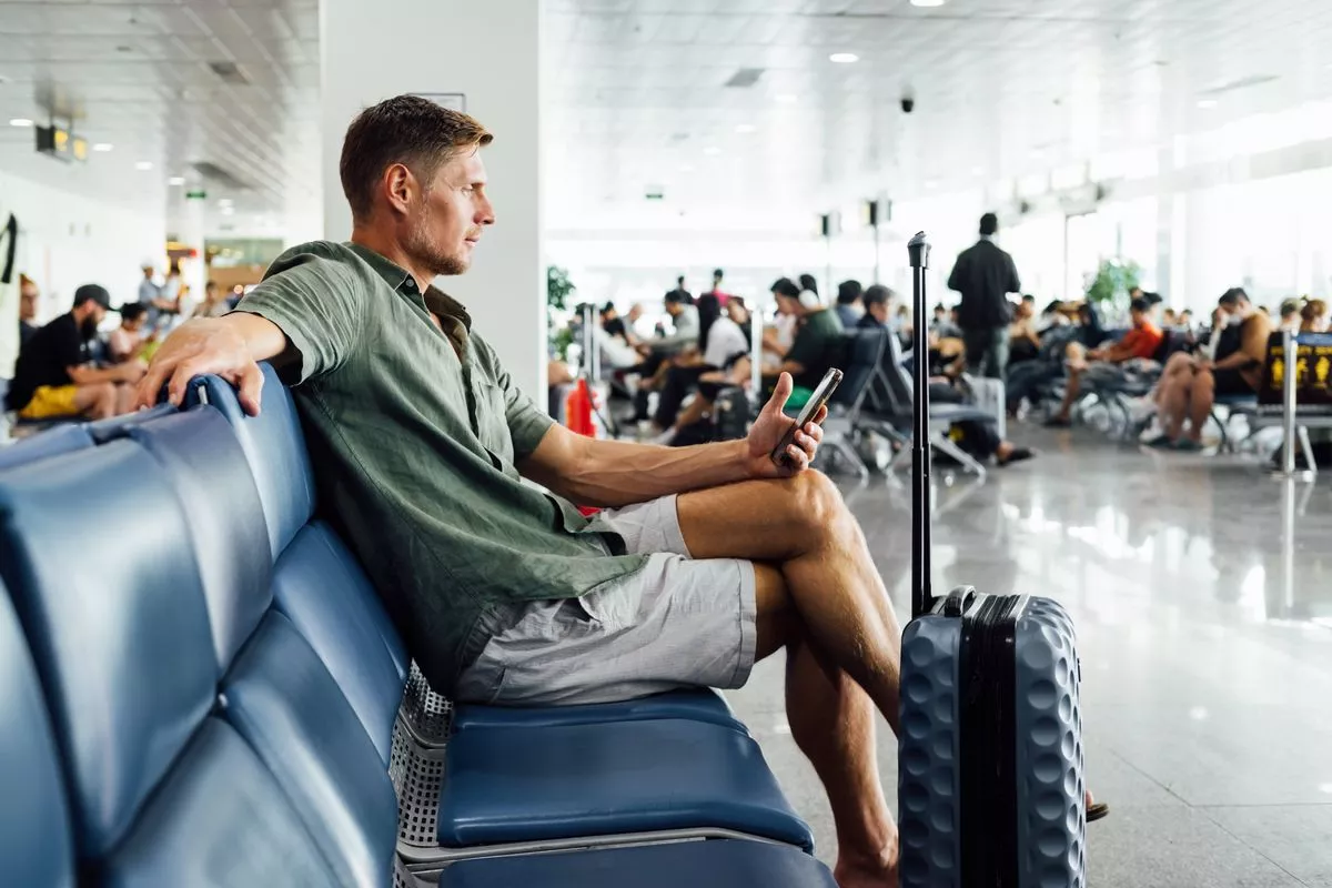 Casual mature man with smartphone waiting at airport terminal seating area