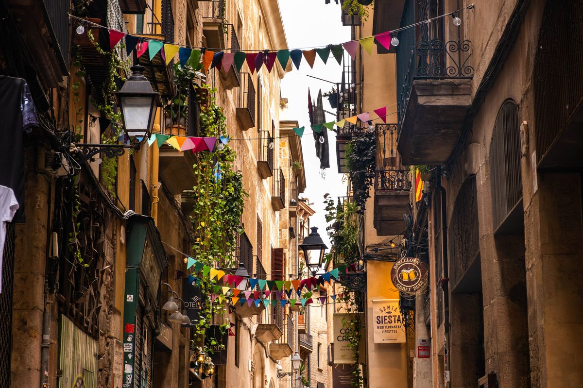 A charming alleyway in Barcelona is adorned with vibrant flags and greenery, capturing the spirit of Mediterranean festivity.
