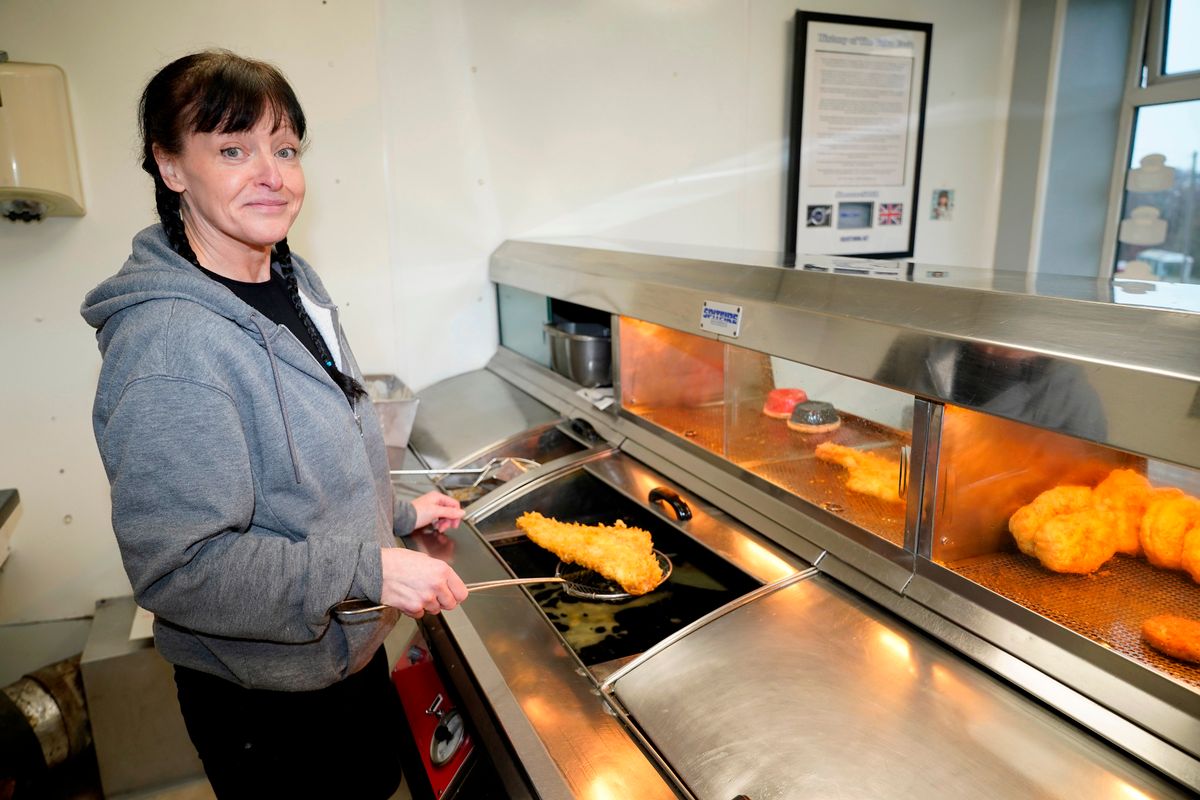Sam stands behind the counter serving a big piece of battered fish