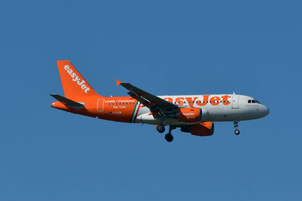 An orange and white commercial airplane with the word "easyJet" on its fuselage is flying in the clear blue sky, with its landing gear extended.