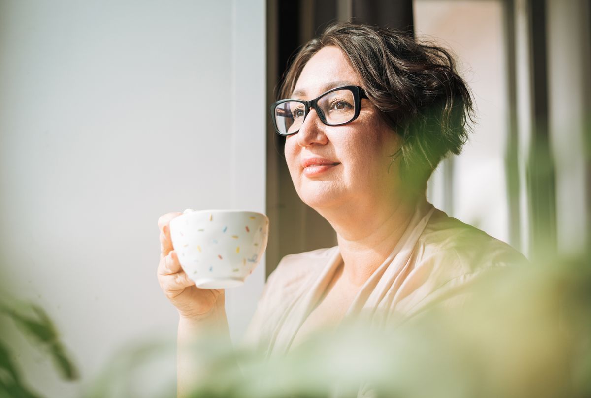 A beautiful middle-aged woman drinks coffee and looks out the window of her house