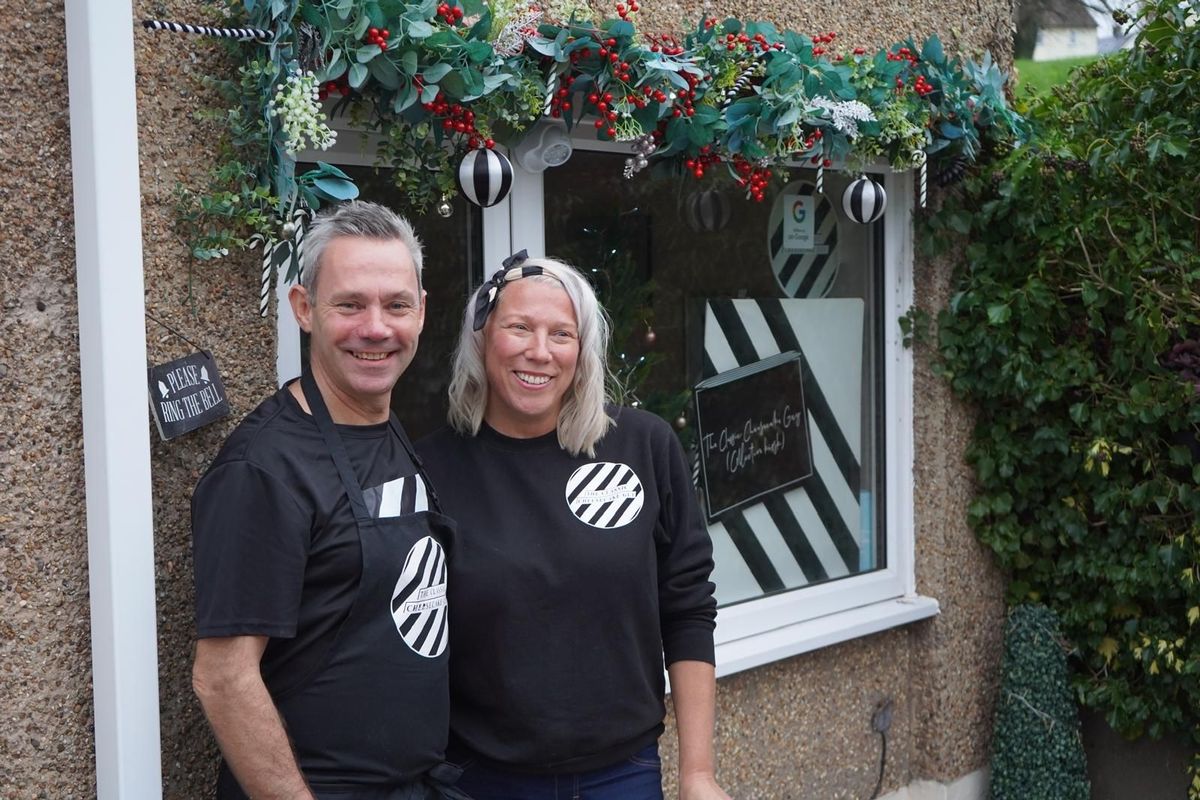 Man and woman stood outside window of home both dressed in black clothing.