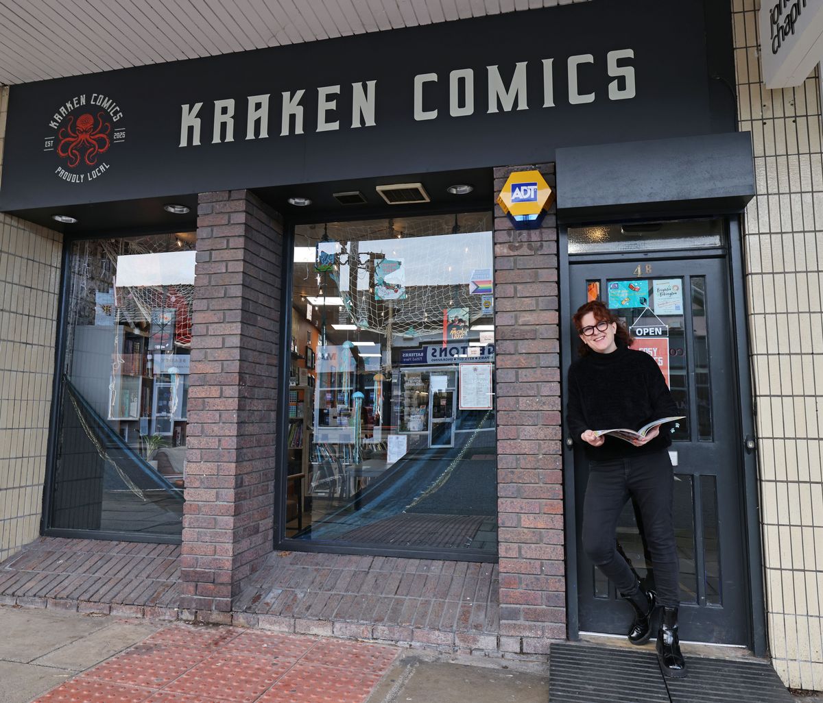 Cathy Charnley stands outside Kraken Comics on Church Road in Bebington. She is dressed in black and holding a book