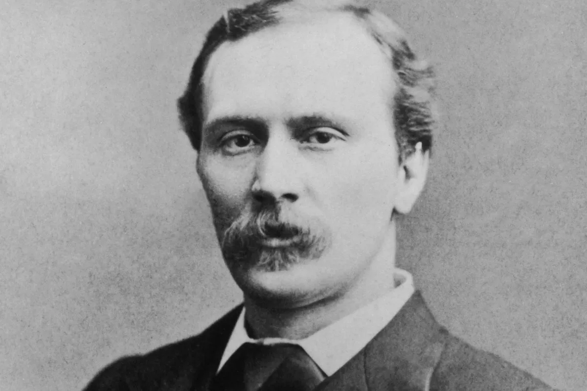 Portrait photograph in black and white of a man in a smart three-piece suit and tie with a brooch. A long moustache droops over his lip. His hair is cropped short in a tight side part.