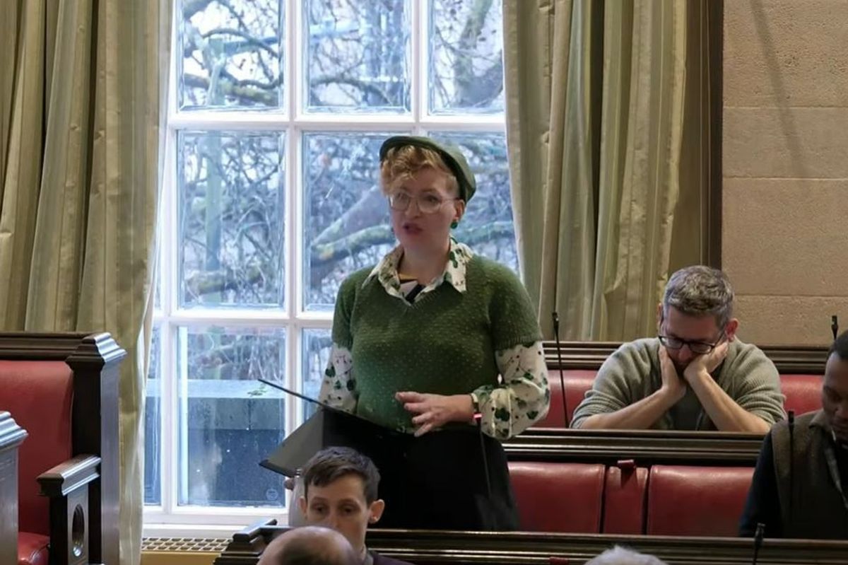 Woman wearing green jersey stood up delivering speech in council chamber
