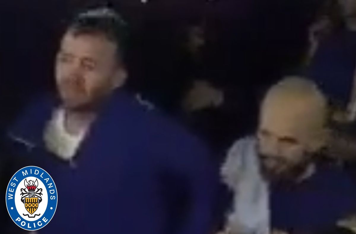 CCTV image of a white man with a trimmed beard, with short brown hair and appears to be wearing a royal blue top over a white-t-shirt and a second man, who is white, and bald with a thick, brown beard, wearing a royal-blue t-shirt and a white top, slung over his shoulder