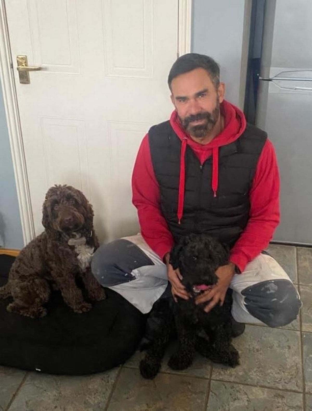 A man with dark hair kneeling down with two dogs