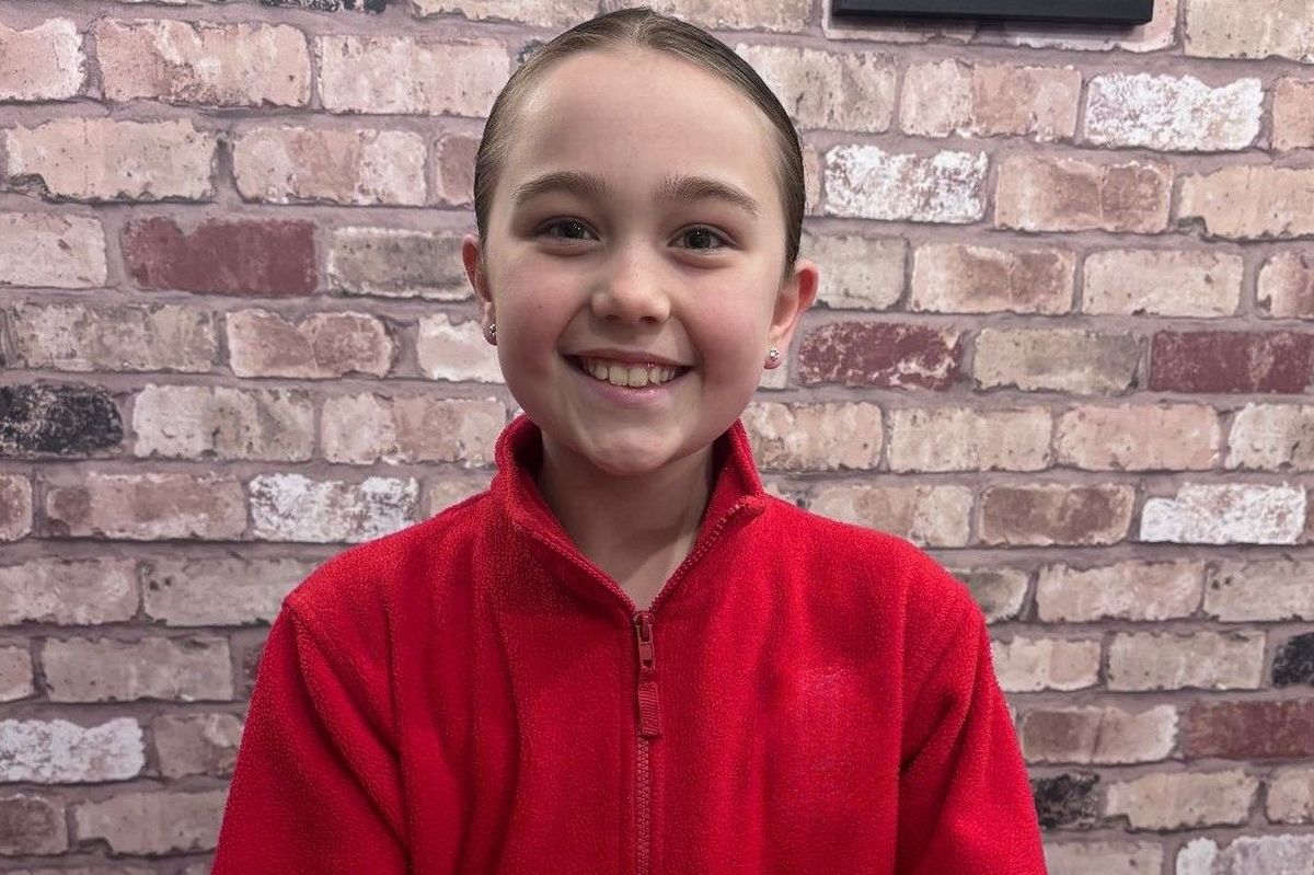A girl aged nine, dark hair in a ponytail wearing a red fleece, she is holding a rock in her hand