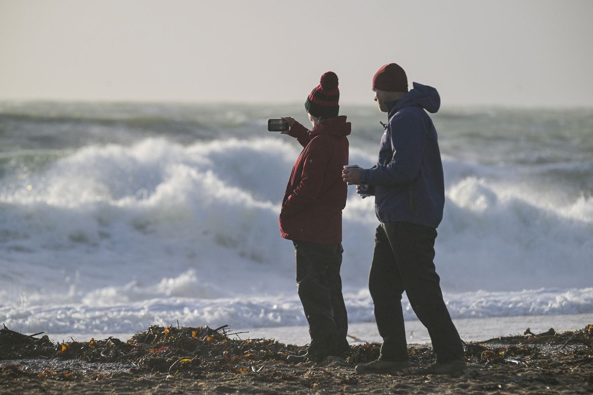 Early morning walkers watch large waves caused by the arrival of Storm Ingrid at Gyllyngvase Beach