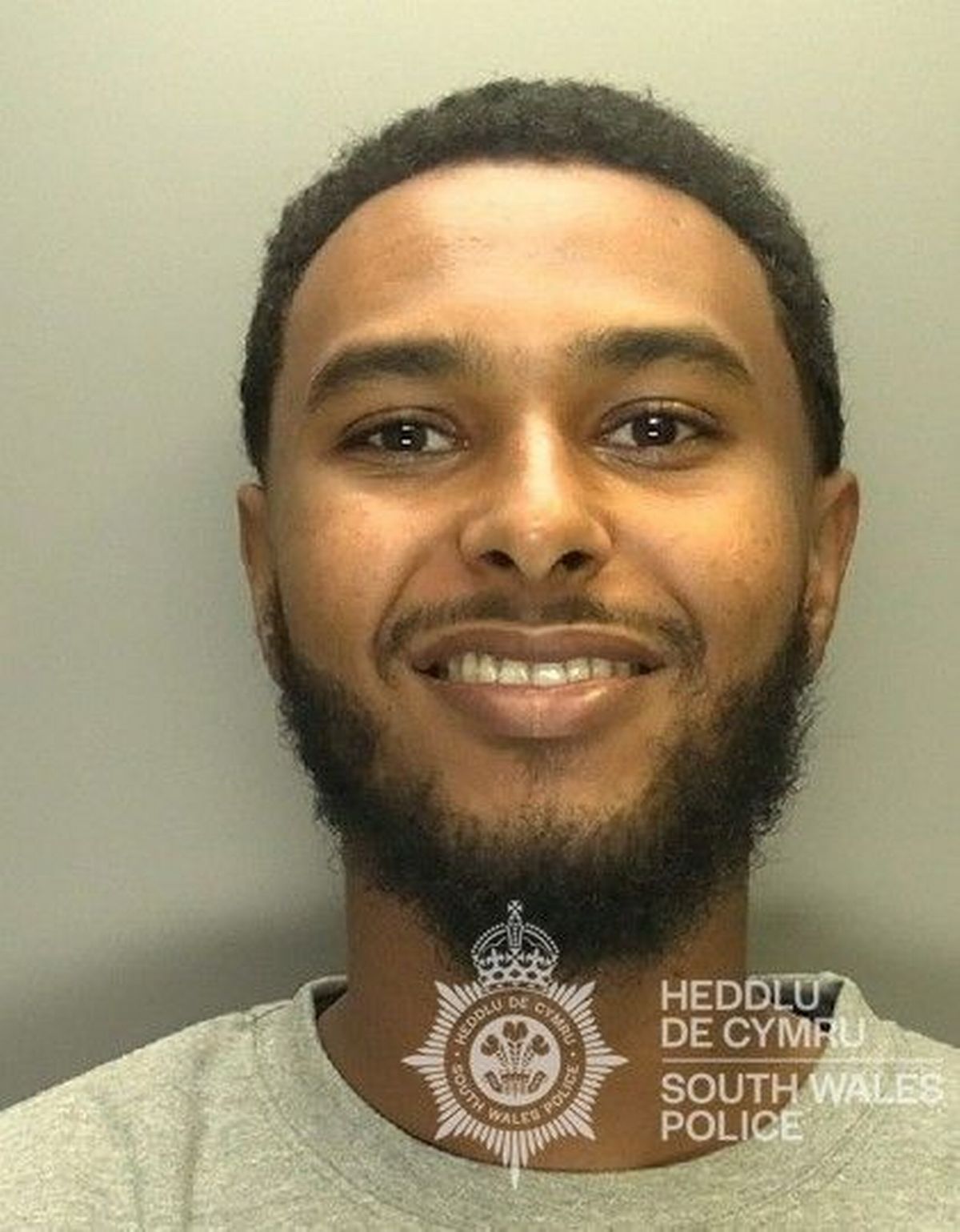 Custody photo of Jamal Hourrieh, 24, who has short black hair, a black beard and is wearing a grey tracksuit