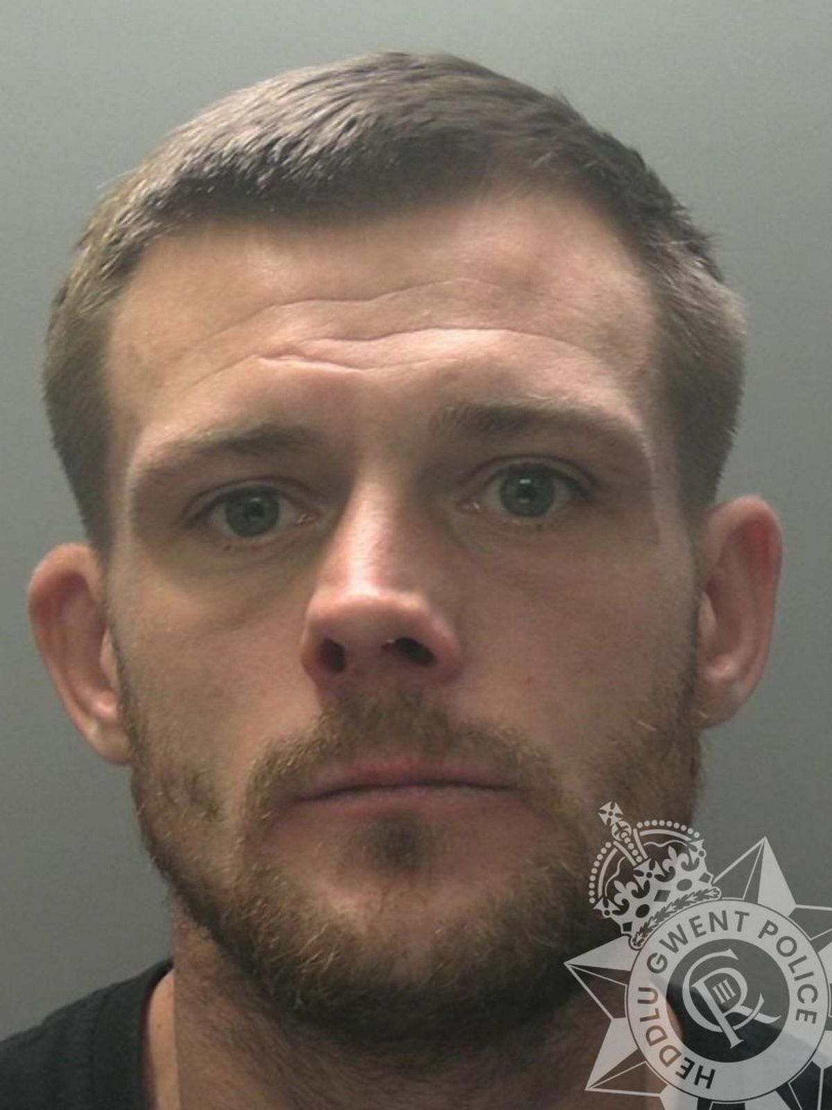 Custody pic of Ryan Axton, 33, who has brown hair, a brown beard and is wearing a black t-shirt.