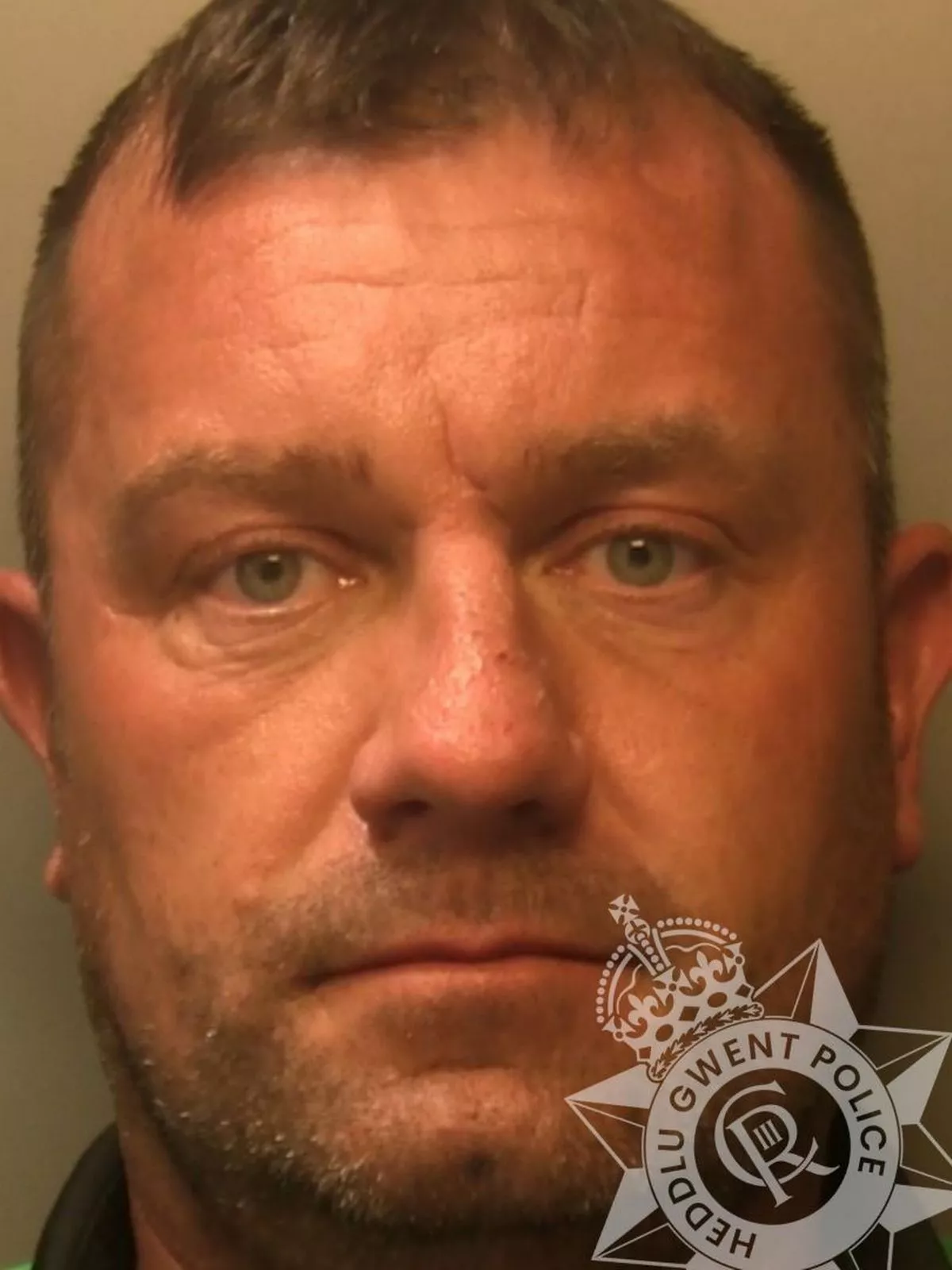 Custody photo of Damien Shearer, 45, who has short brown hair, stubble, and is wearing a top with a black collar