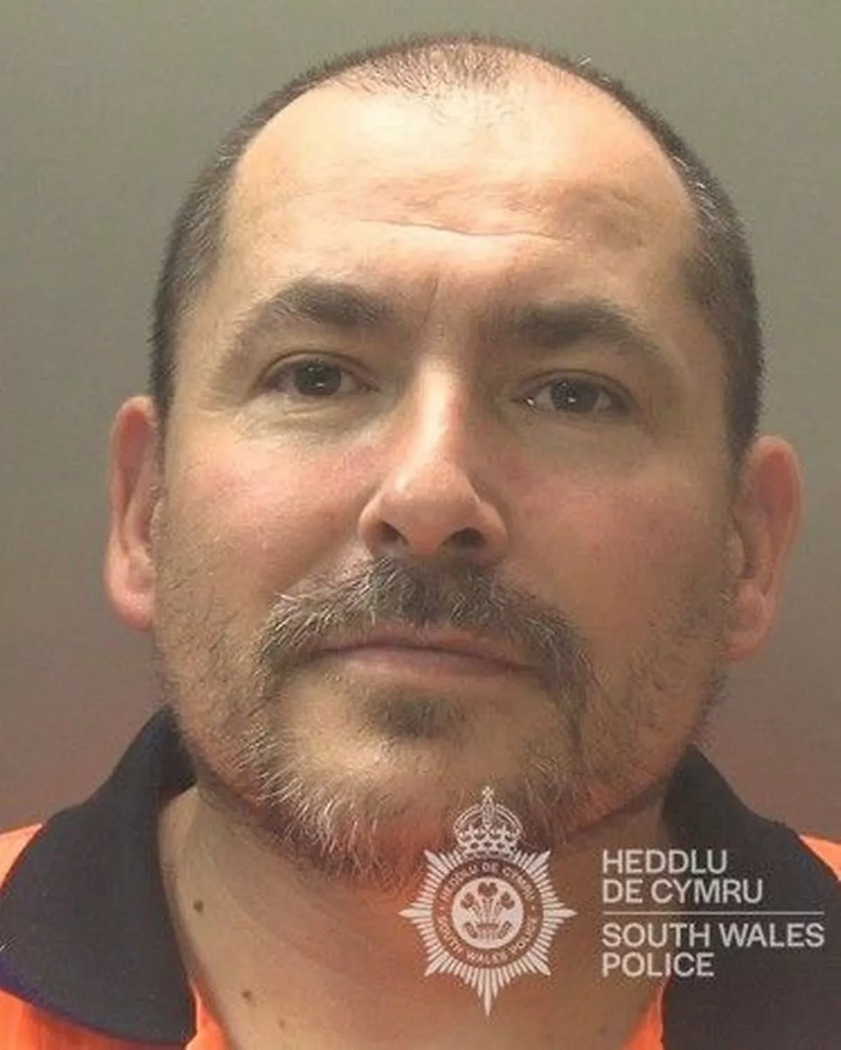 Custody photo of Jason Stafford, 49, who is bald, has a grey goatee and is wearing an orange shirt with a black collar.