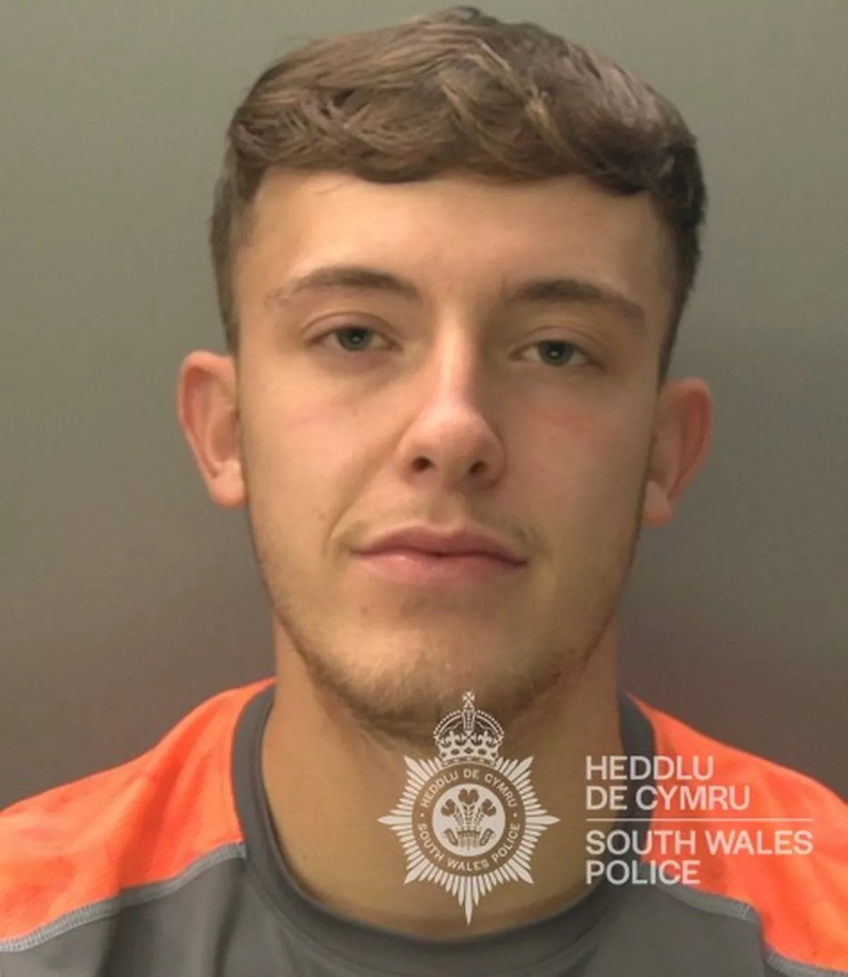 Custody photo of Liam Key, 23, who has short brown hair and is wearing an orange and grey t-shirt.