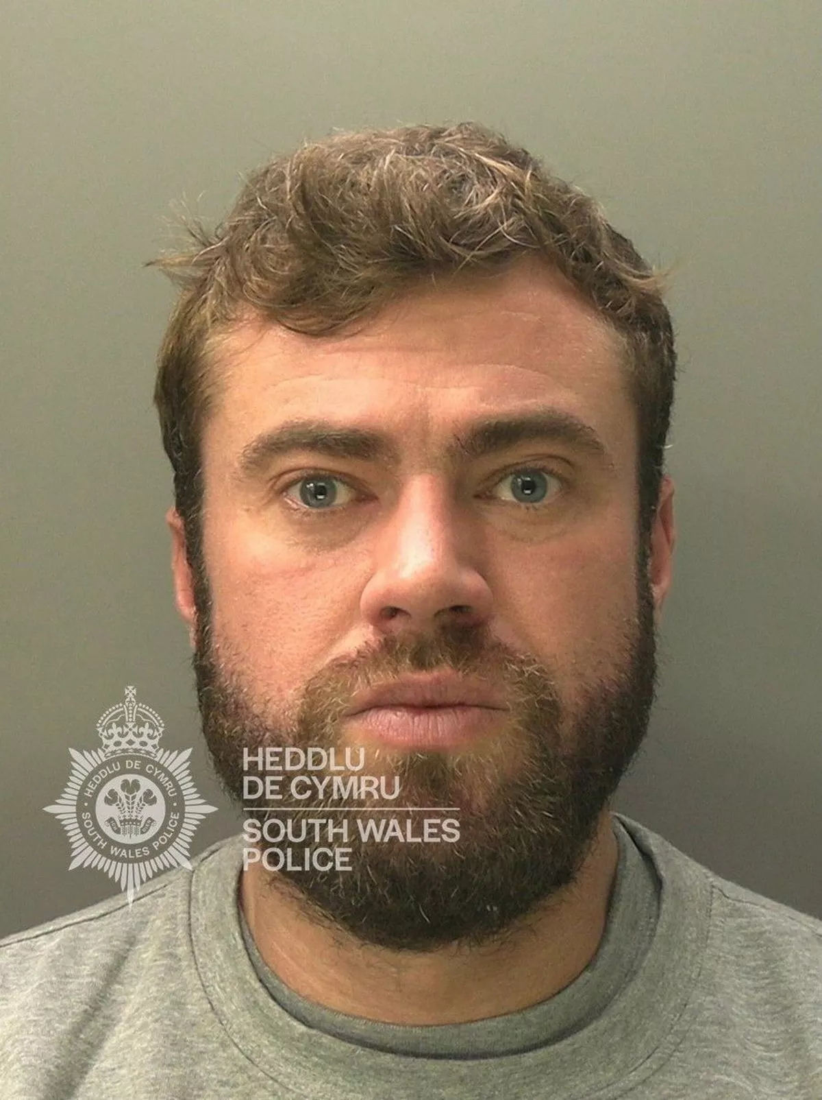 Custody photo of Thomas Griffiths, 34, who has brown hair, a brown beard and is wearing a grey tracksuit.