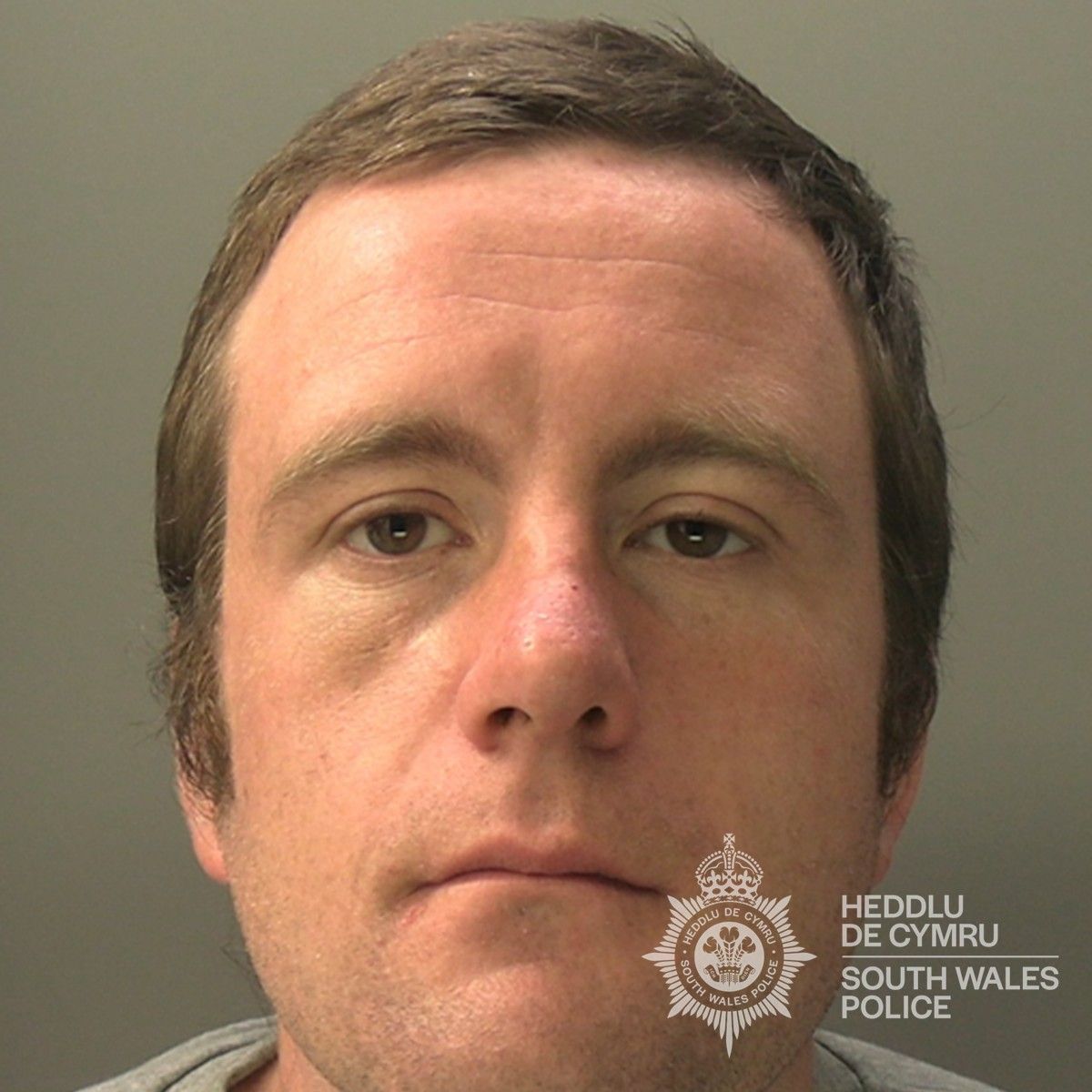 Custody photo of Christopher Moore, 31, who has brown hair and is wearing a grey tracksuit.