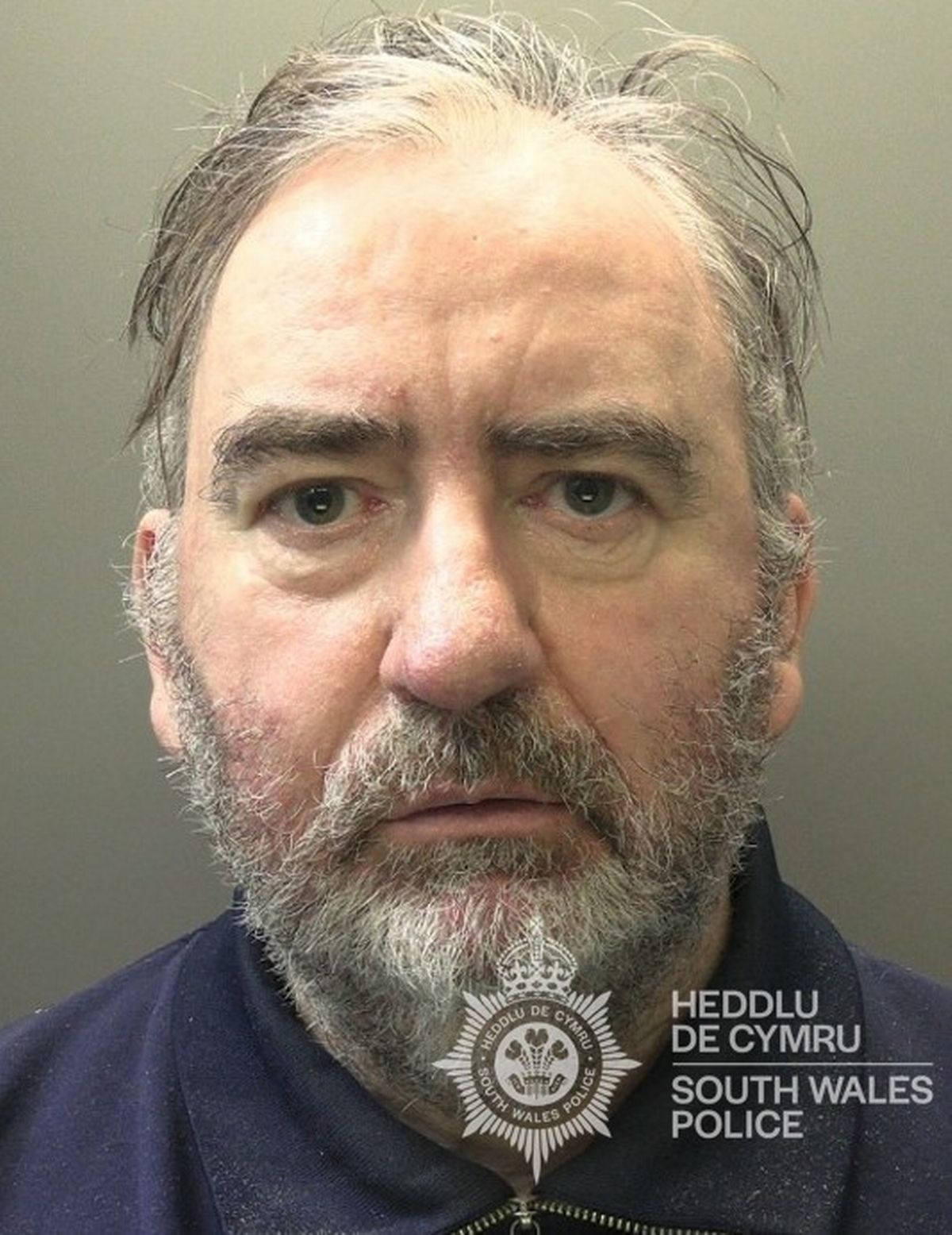 Custody photo of Dafydd Evans, 61, who has grey hair, a grey beard and is wearing a blue jacket.