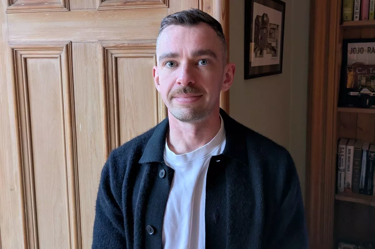 An image of a young man wearing a dark jacket over a white top.