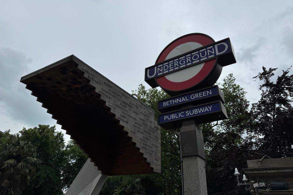 Signs outside Bethnal Green Underground station with the memorial in view 