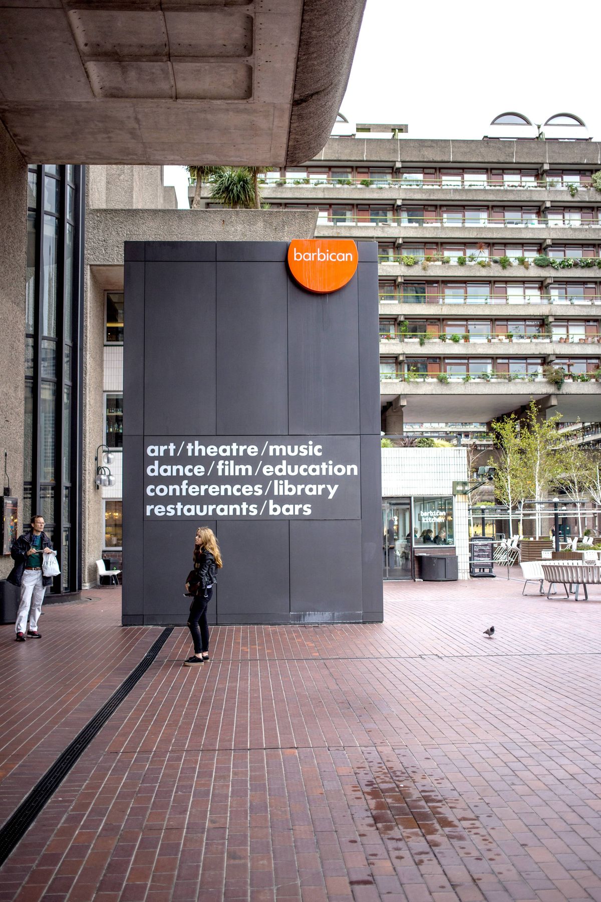 People waiting outside the entrance to the iconic Barbican arts and theatre centre in The City of London. The Barbican in the City of London is a large estate and an iconic new brutalist architecture landmark built in the sixties with the addition of an art and conference centre in the eighties which is the largest in Europe