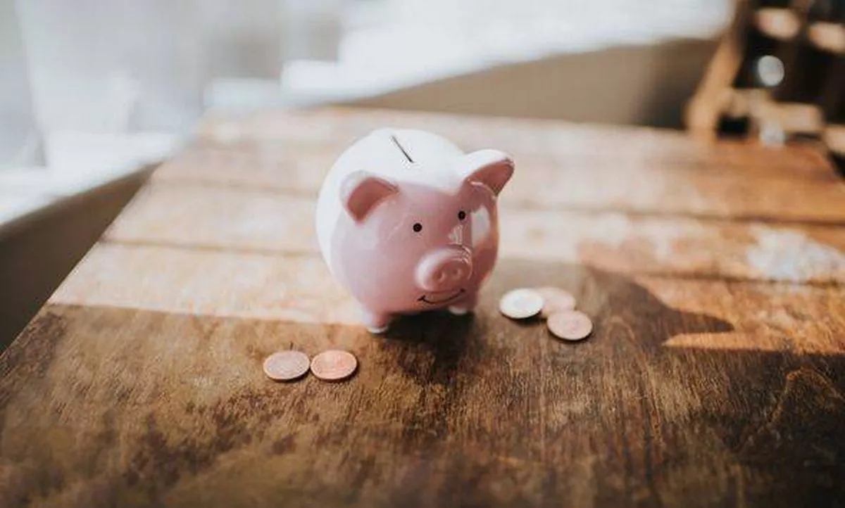 Piggy bank on a wooden table with sunbeams, surrounded by coins. Space for copy.