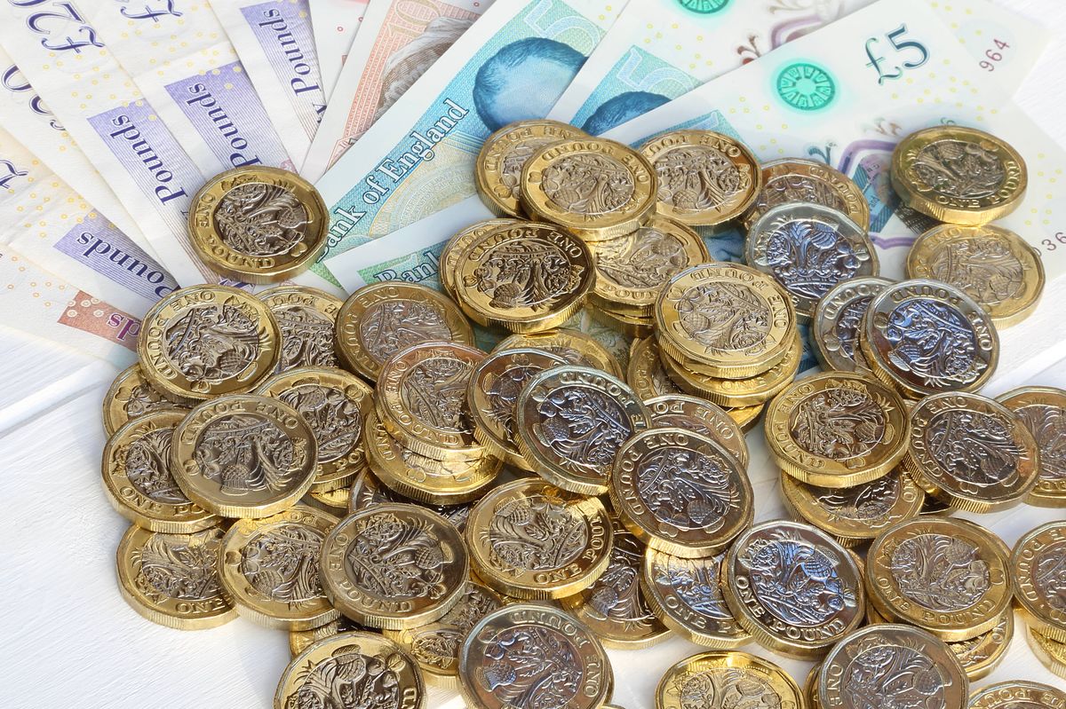 Newly minted British one pound coins scattered on fan of British pound notes, in close-up.