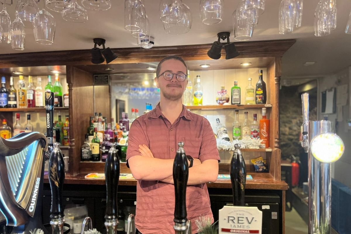 The landlord of a pub stood behind a bar