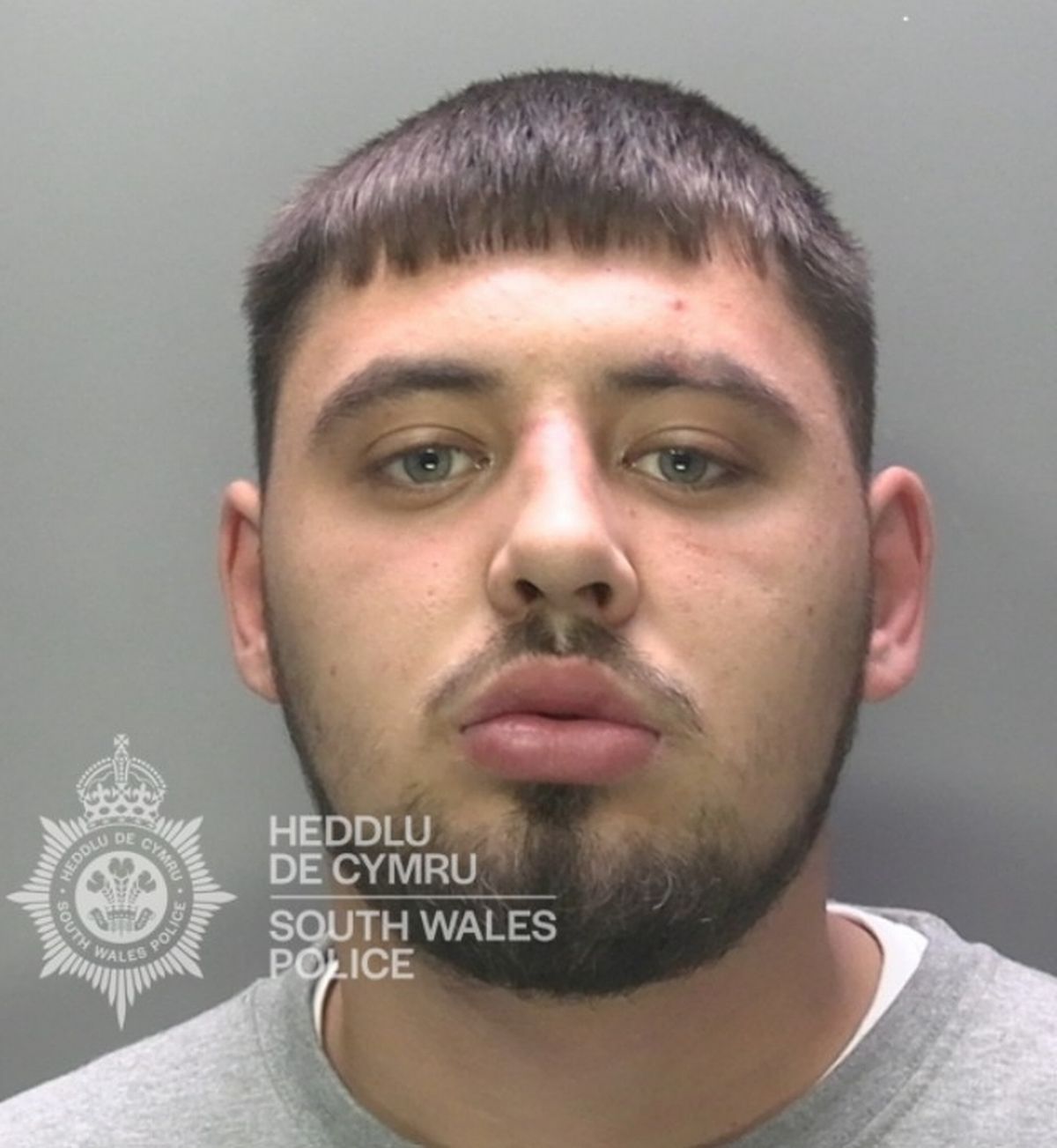 A custody image of a man in his mid-20s with short black hair and blac facial hair