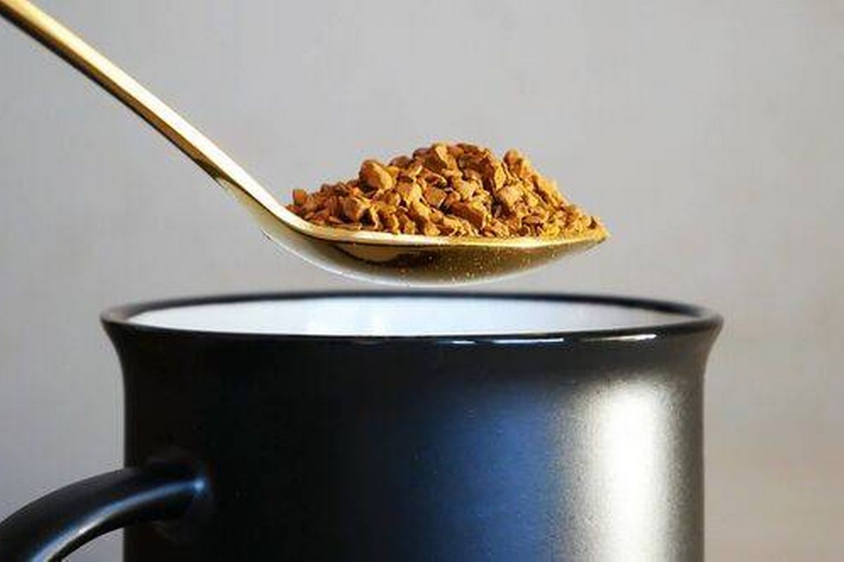 Some freeze-dried coffee on a golden teaspoon above a black cup