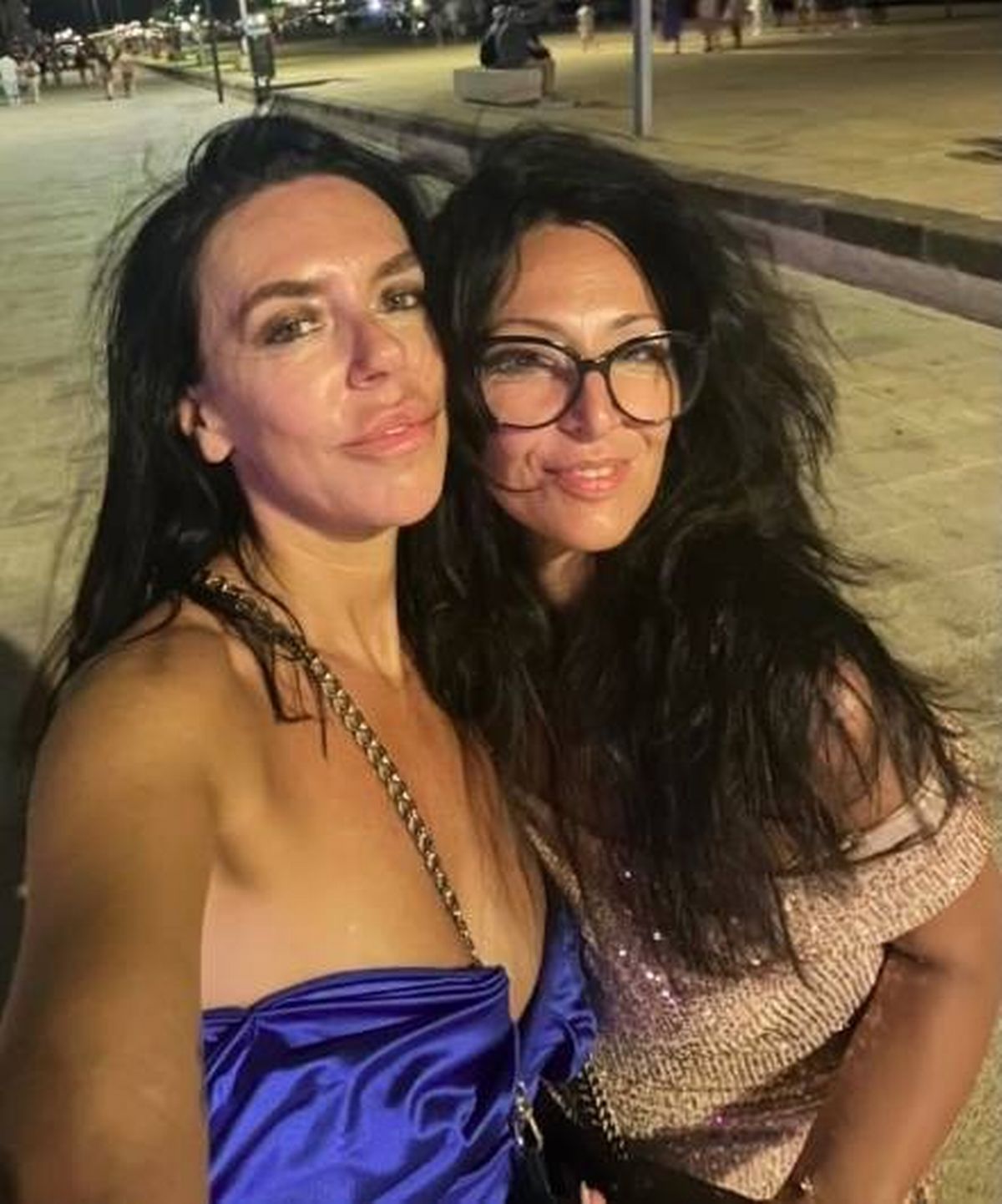 Two women with long black hair are smiling and posing for a photograph, one of them wearing glasses.