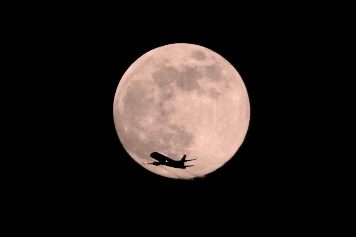 A plane passes in front of a Wolf Supermoon, Friday, Jan 2, 2026, in Chicago. (AP Photo/Kiichiro Sato)